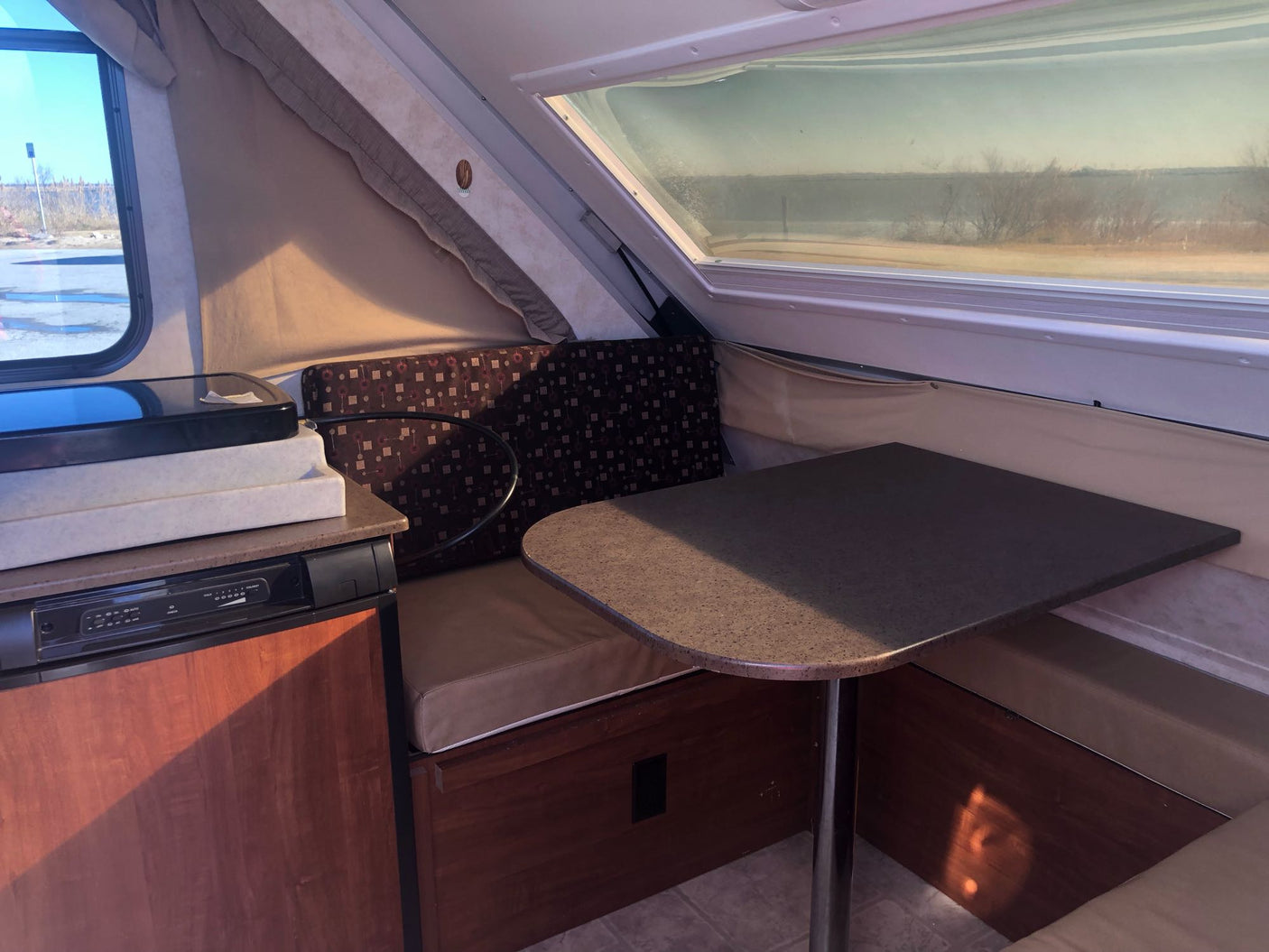parked on a sunny driveway.|White Tesla Model Y towing a compact A-liner pop-up camper in a driveway