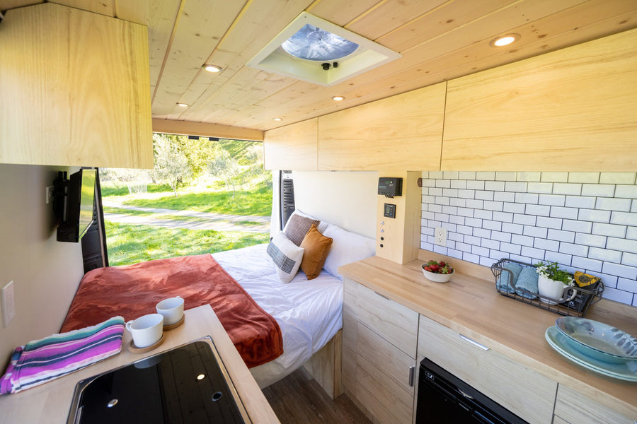Bright RV rental interior: A cozy bed, compact kitchen, and smart storage solutions for comfortable travel.