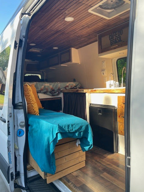 Cozy RV rental camper van interior with a bed, kitchen with sink, wooden ceiling, and flooring. Ideal for mobile living.