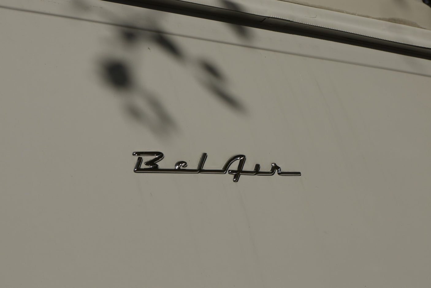 with a chrome winged hood ornament & wipers. Trees reflect in the windshield.|Sleek chrome hood ornament