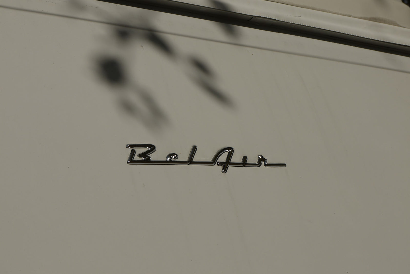 with a chrome winged hood ornament & wipers. Trees reflect in the windshield.|Sleek chrome hood ornament