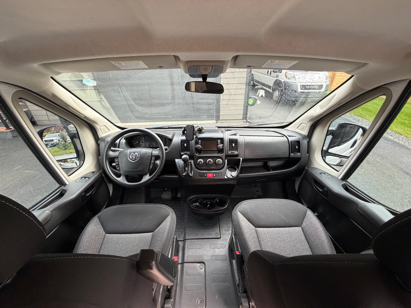 Inside an RV rental camper van: front cabin showing dashboard, steering wheel, seats, and outside view through the windshield.