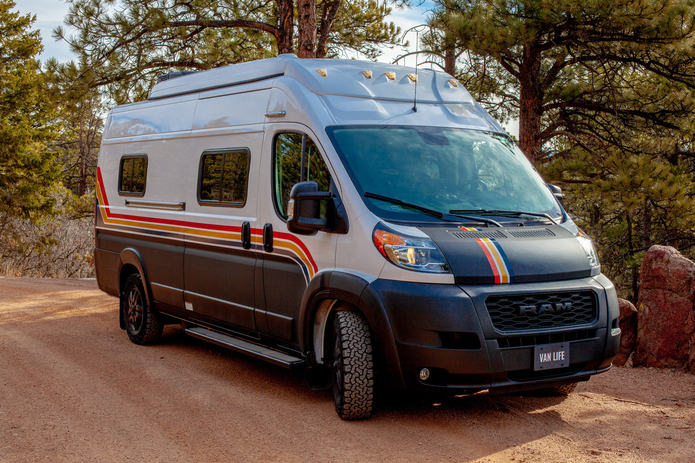 Adventure-ready custom camper van RV rental on a dirt road amidst pine trees. Perfect for your next outdoor road trip!