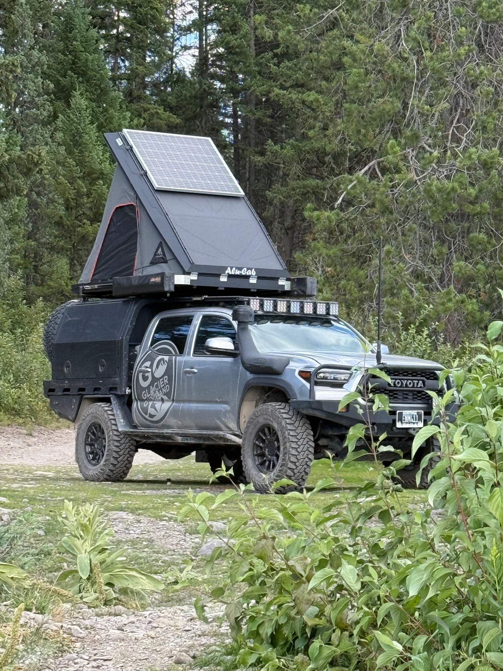 Grey Toyota Tacoma overlanding truck with rooftop tent, solar panel, and off-road gear. Ideal for your next rv rental adventure.
