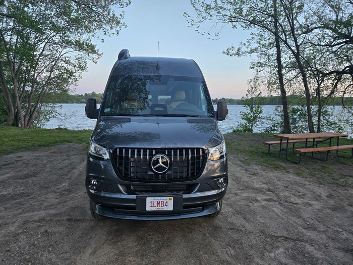 A sleek Mercedes Sprinter campervan, ready for your RV rental getaway, parked lakeside next to a picnic table.