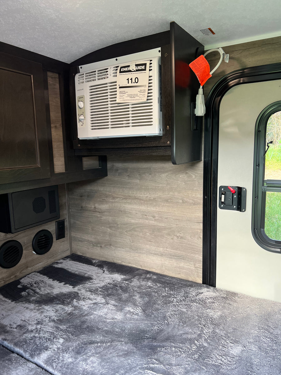Inside an RV rental: a compact living space featuring a wall-mounted AC, comfortable bedding, and practical cabinetry.