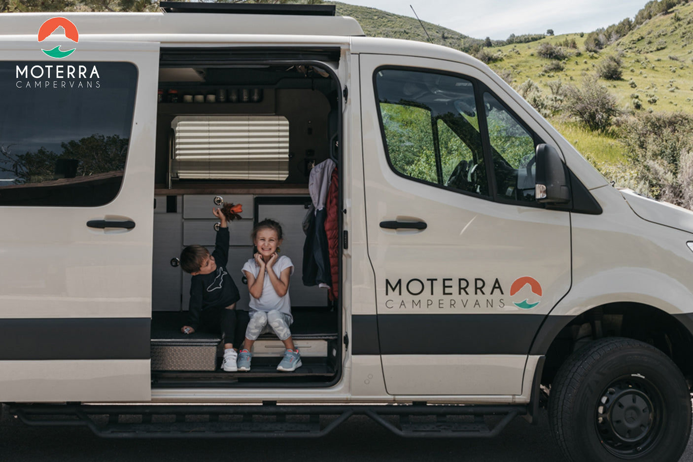 Two smiling kids enjoy the spacious interior of a Moterra RV rental camper van, ideal for family trips and adventures.
