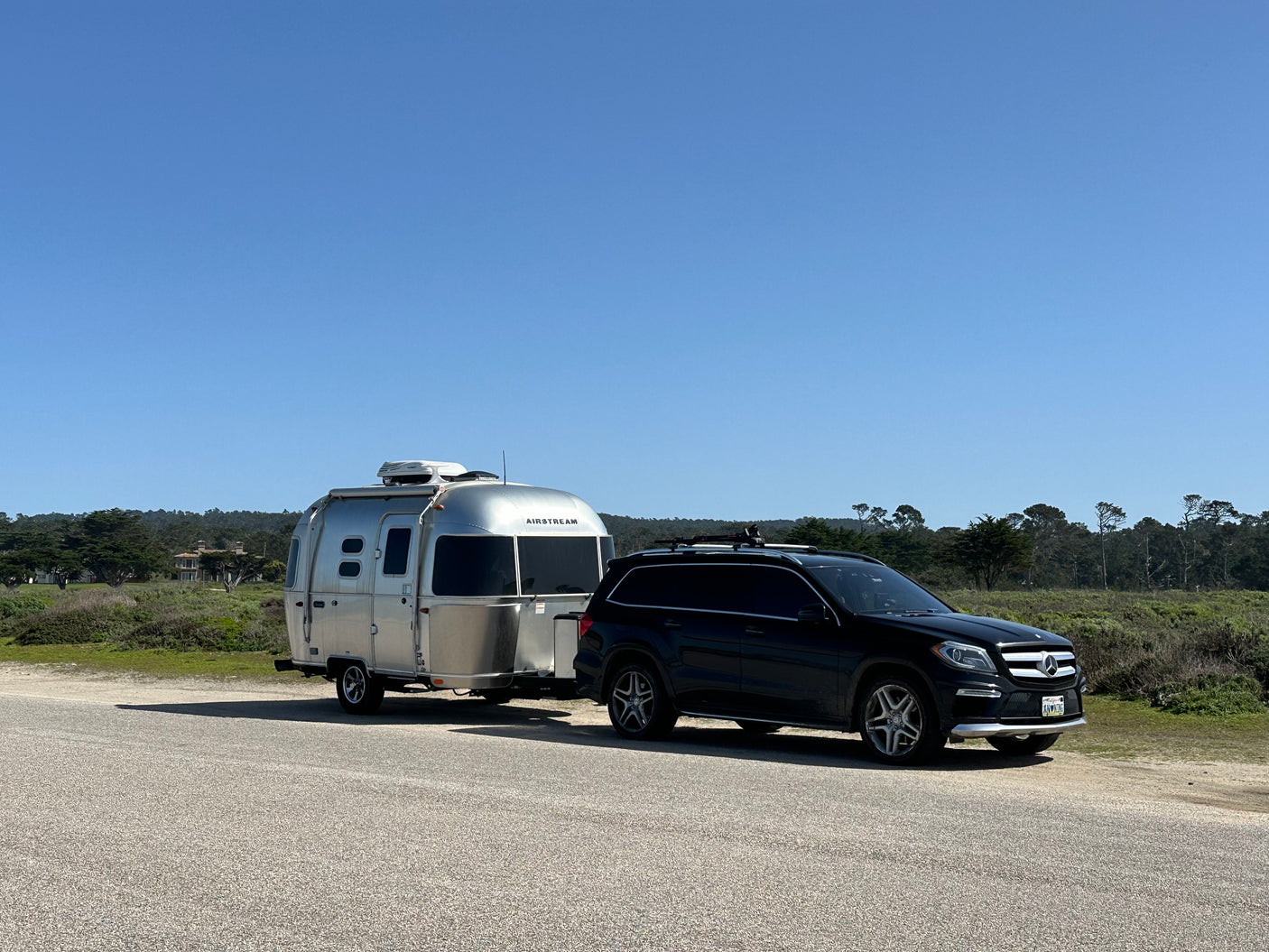 A black Mercedes SUV tows a silver Airstream travel trailer on a sunny day. An ideal RV rental for your next adventure.