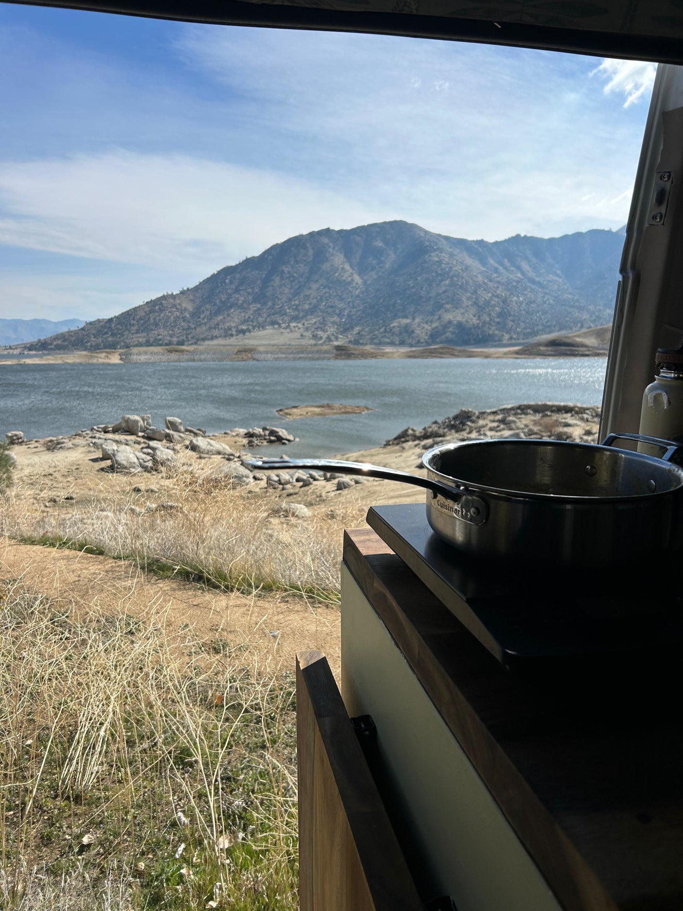 RV rental view: cooking with a lake & mountains backdrop. Enjoy van life with scenic outdoor cooking from your camper.