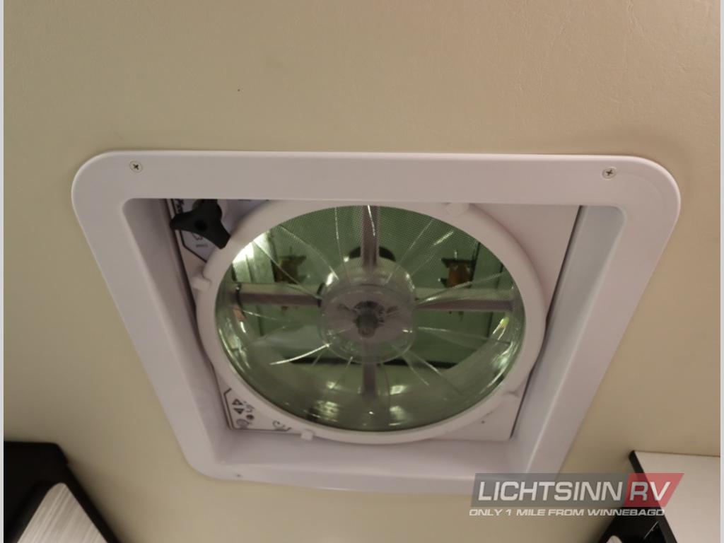 RV rental: Overhead clear vent fan providing fresh air circulation in a camper's ceiling.