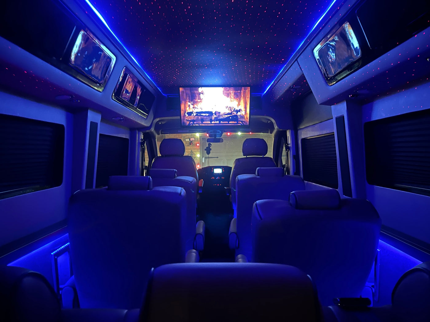 Interior of a luxury rv rental with vibrant blue lighting, a starry ceiling, and a screen displaying a fireplace. — photo 13