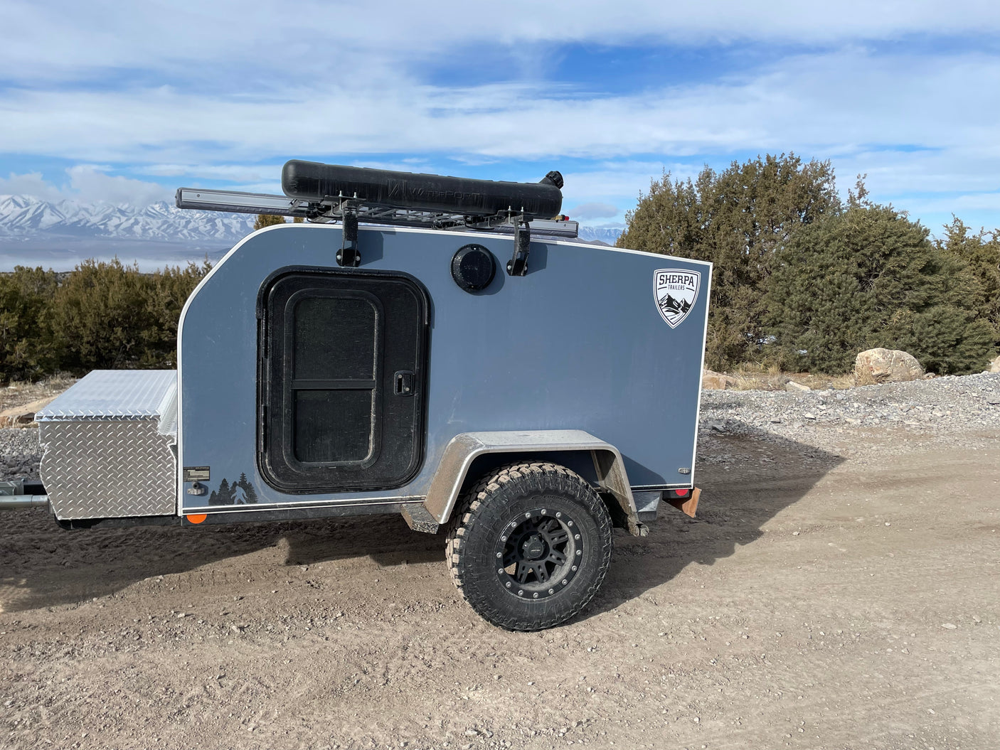 Grey off-road teardrop camper ready for your RV rental mountain adventure. Features diamond plate storage & roof rack.