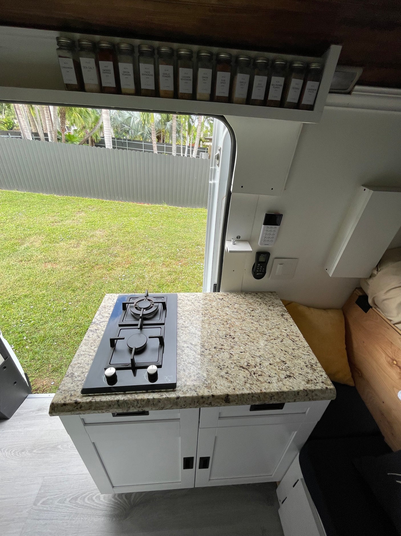 RV rental: A compact van kitchen featuring a built-in stove, granite countertop, spice rack, and an open door view to a green yard.