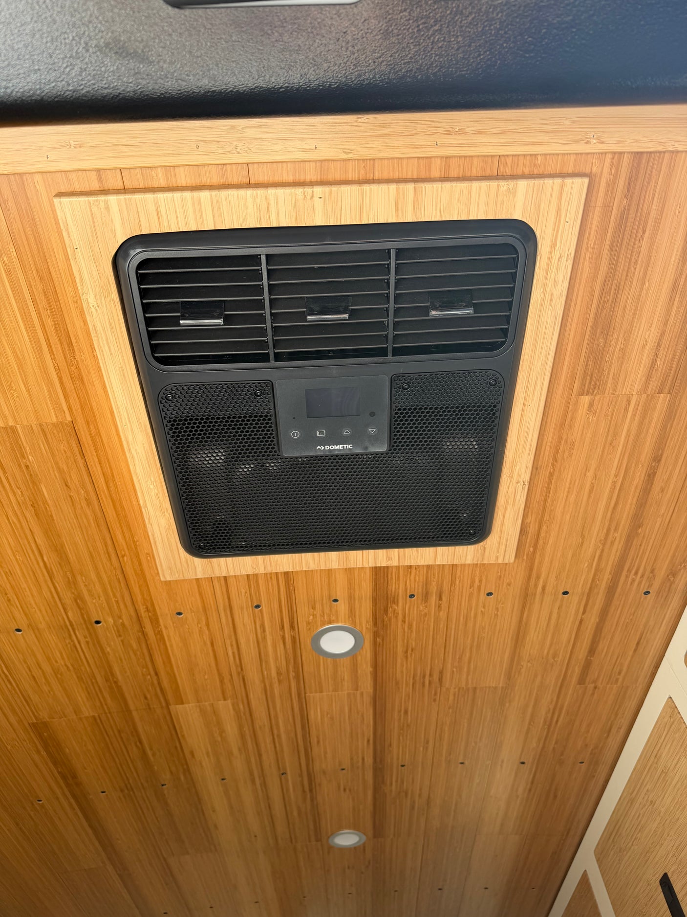 Overhead Dometic AC unit installed in a light bamboo ceiling of an rv rental, providing air conditioning for the van interior.