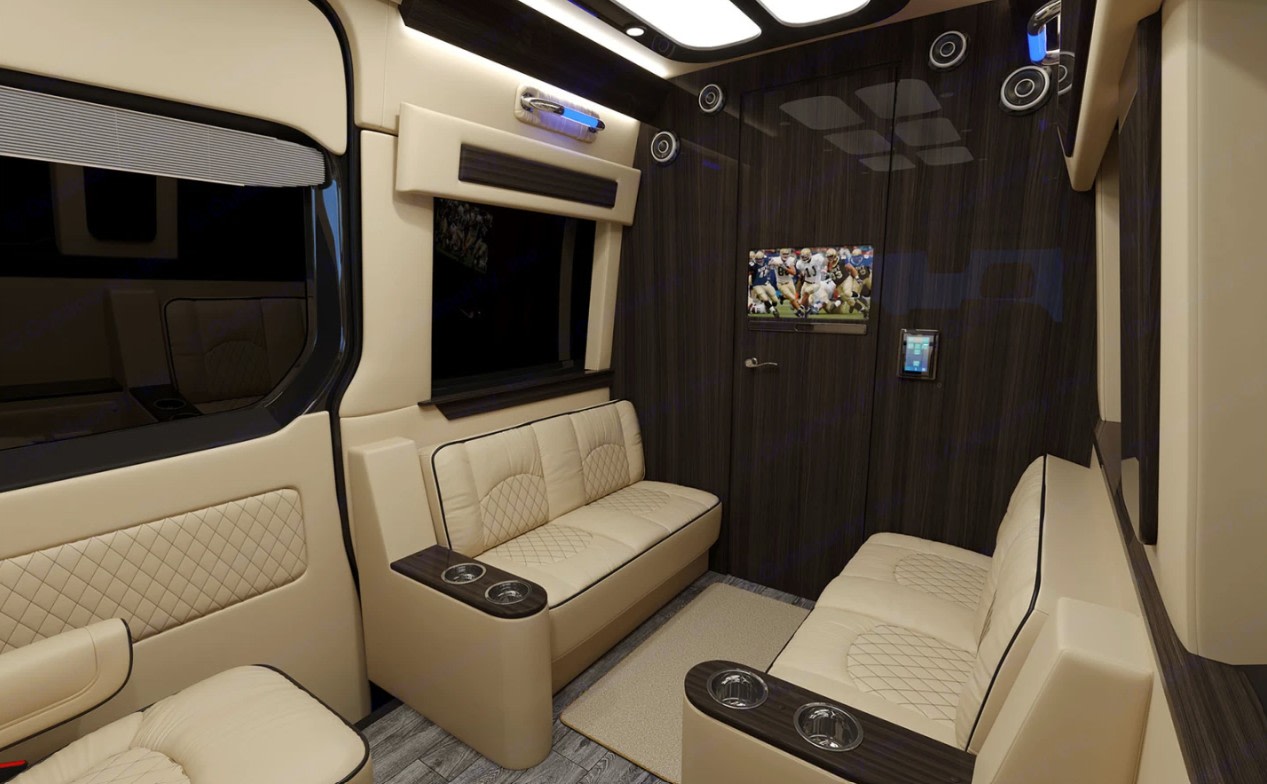 Luxury RV rental interior featuring plush beige seating, TV showing football, and a wall tablet control panel.