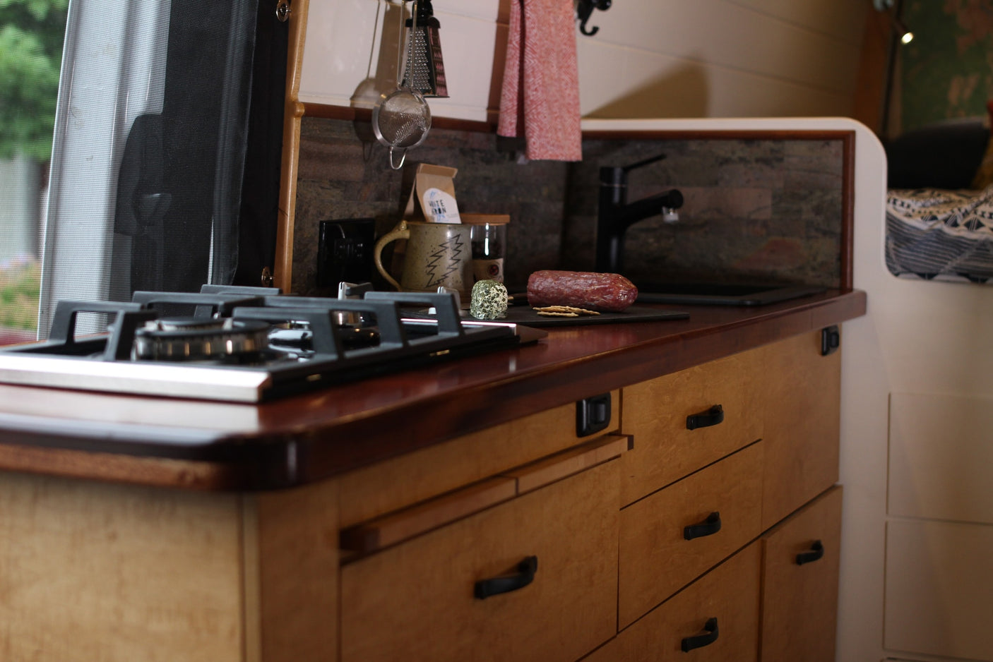 Inside an RV rental: a modern kitchen with a gas stove, wood counter, sink, and a charcuterie setup, ready for adventure.
