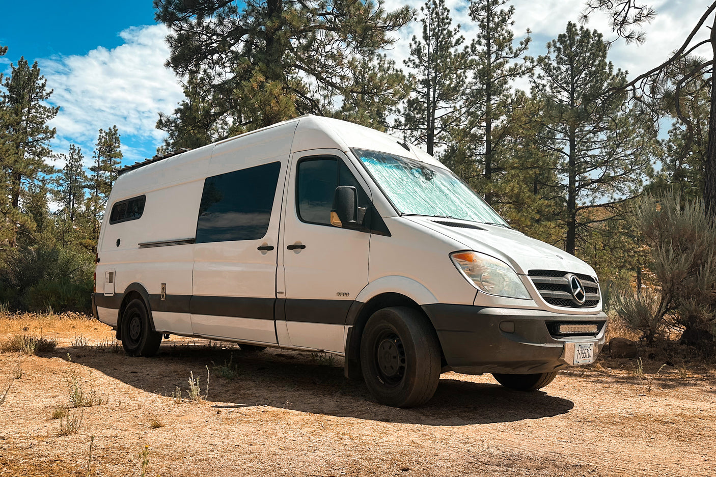 White Mercedes Sprinter rv rental camper van parked in a sunny, scenic forest. Great for outdoor adventures.