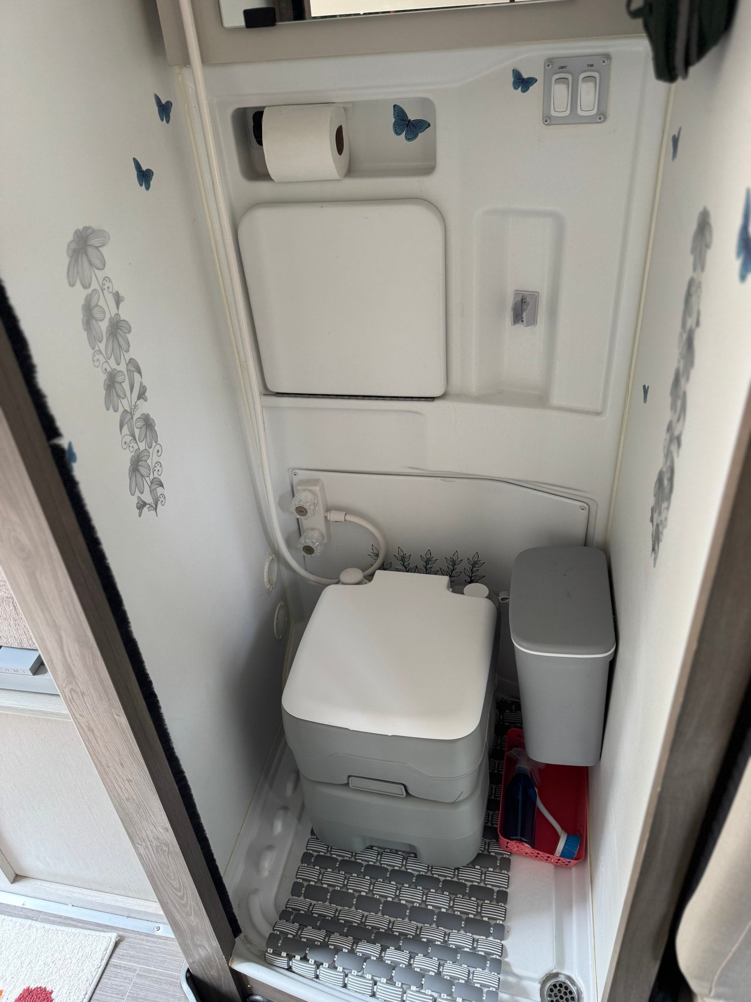 Inside an RV rental's compact wet bath featuring a portable toilet, shower, and decorative details.