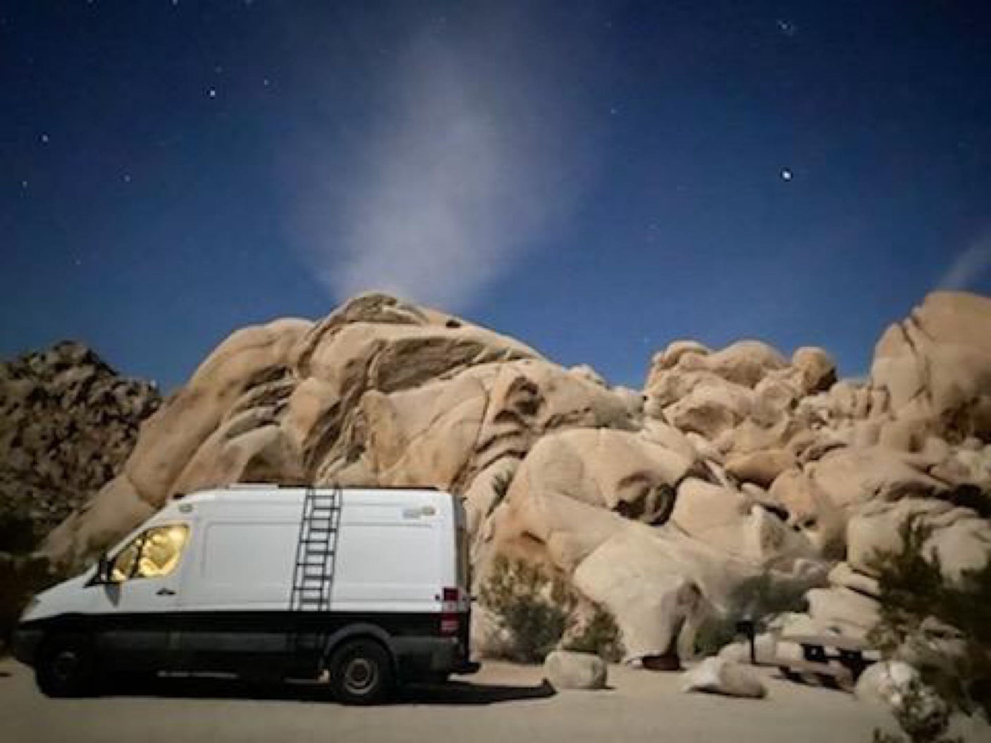 Night camping in an RV rental van nestled among large rock formations under a starry desert sky. Adventure awaits!