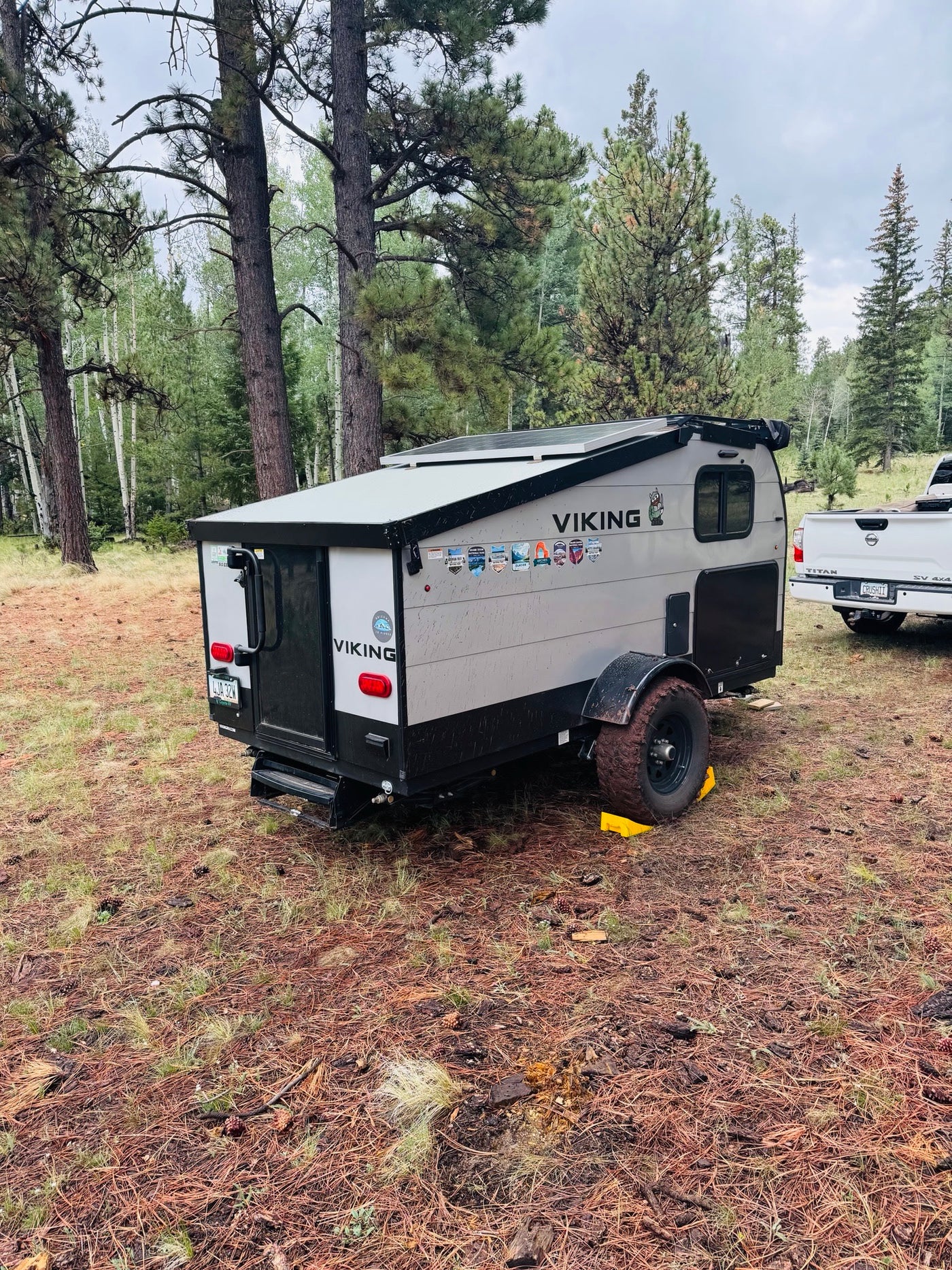 among tall pine trees. Perfect for your next adventure!|Compact RV rental camper parked in a rustic forest campsite with a truck nearby. Perfect for outdoor adventures!|This compact Viking RV rental camper is set in a peaceful pine forest — photo 1