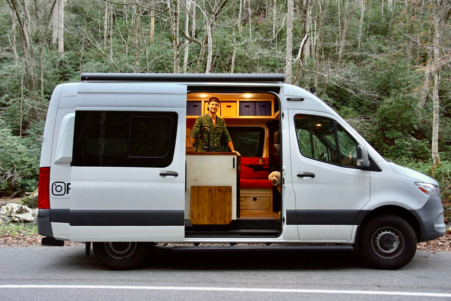 RV rental ready for adventure: A man and his dog in their customized camper van in a forest setting.