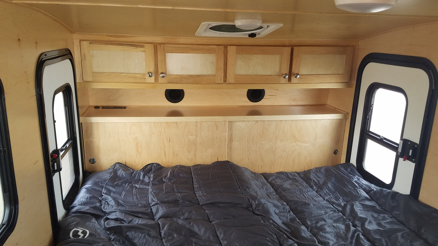 RV rental's light wood interior with bed, overhead storage, and side windows. A compact, cozy sleeping space.