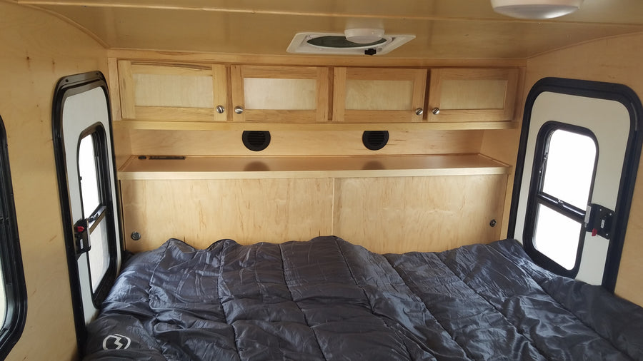 RV rental's light wood interior with bed, overhead storage, and side windows. A compact, cozy sleeping space.