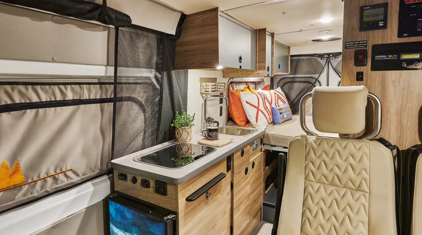 An RV rental's inviting interior with a compact kitchen, bed, and smart controls for comfortable adventures.