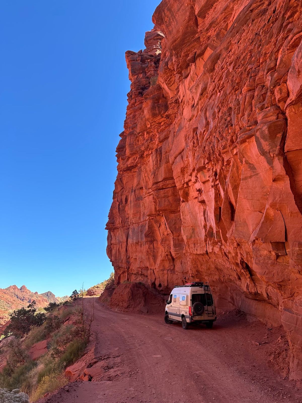dwarfed by a massive red rock cliff under a clear blue sky — photo 5