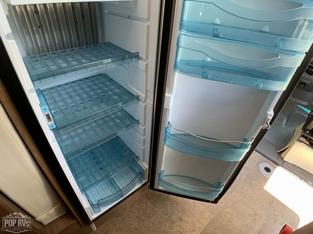 Inside an RV rental refrigerator, showing clean, empty interior with clear grid shelves & blue door bins, ready for groceries.