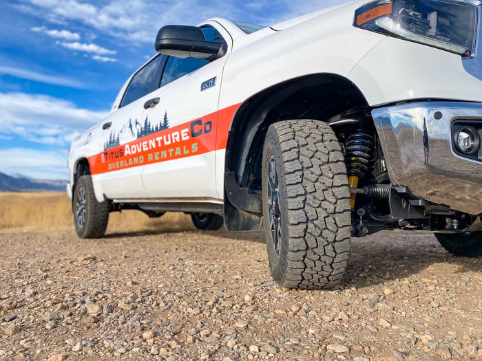 an ideal RV rental for off-grid camping.|Angled view of a white Titus Adventure Co. overland truck on a gravel road. Perfect for your RV rental adventure.|Rear interior of a clean vehicle: black leather seats