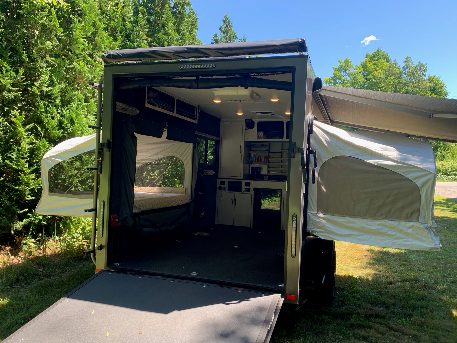 Open adventure trailer ready for your rv rental camping trip, featuring beds & a kitchen setup amidst nature.