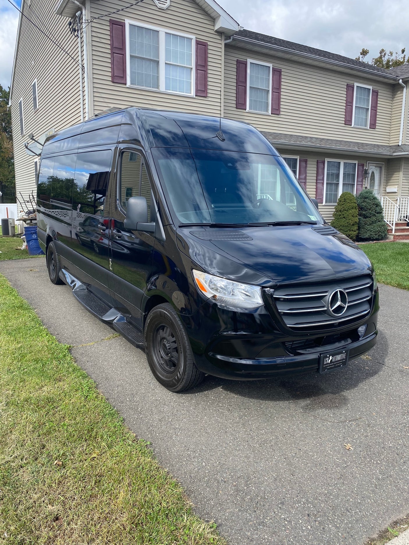 Sleek black Mercedes Sprinter van, ideal for RV rental, parked on a suburban driveway by a house.