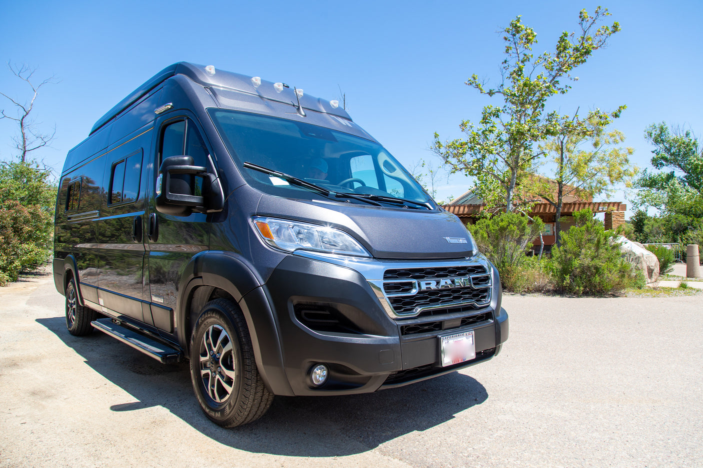 This dark grey Winnebago camper van, perfect for an rv rental, is parked in a sunny park setting.