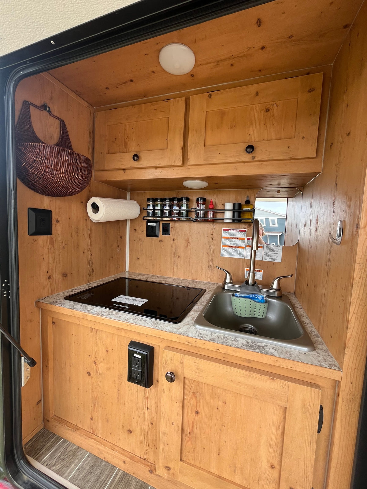 Detailed view of an RV rental's cozy wood-paneled kitchenette with sink, Dometic cooktop, and spice rack. — photo 11