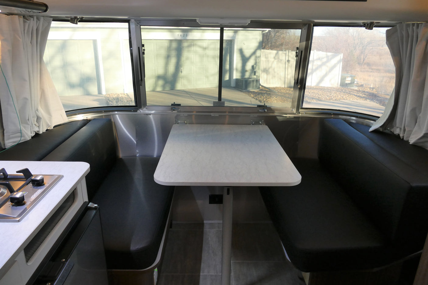 RV rental: Bright interior of a travel trailer, featuring a modern dinette with black benches, a white table, and a kitchen stove.