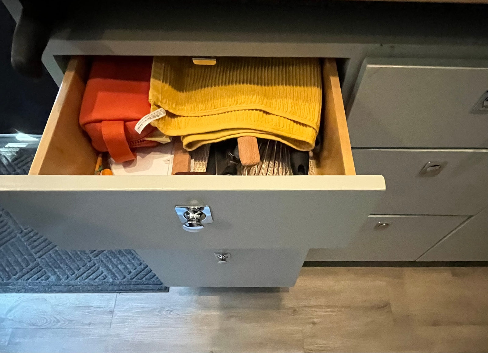 RV rental: Open kitchen drawer with a yellow towel, orange pouch, and utensils, highlighting practical storage.
