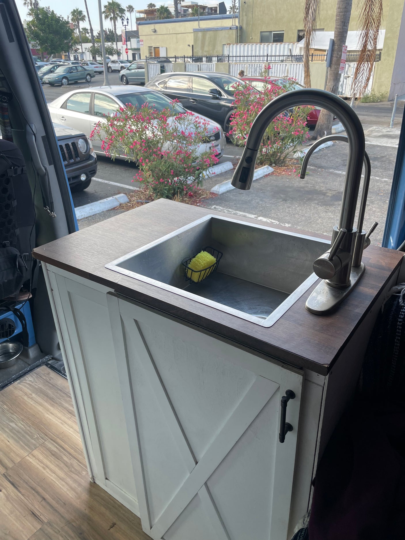 Modern kitchen setup in an rv rental camper van, with a stainless steel sink, wood counter, and white cabinet.