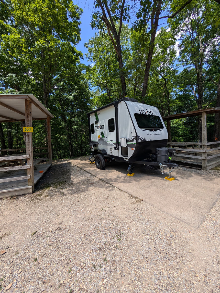 White No Boundaries RV rental at a shaded campsite with a picnic shelter, ready for outdoor adventure.