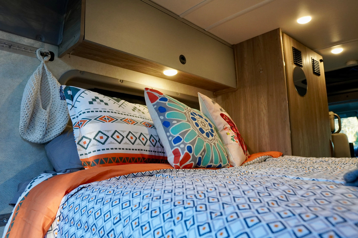 Experience comfort in your RV rental: a neatly made bed with vibrant patterned pillows and warm lighting in a cozy interior.