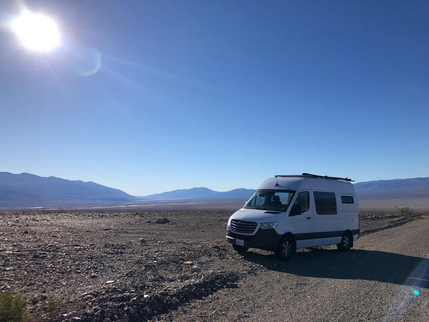 parked by a green field with a Starlink dish and scenic mountain backdrop.|Sunny desert adventure with an RV rental! White camper van on a gravel road — photo 3