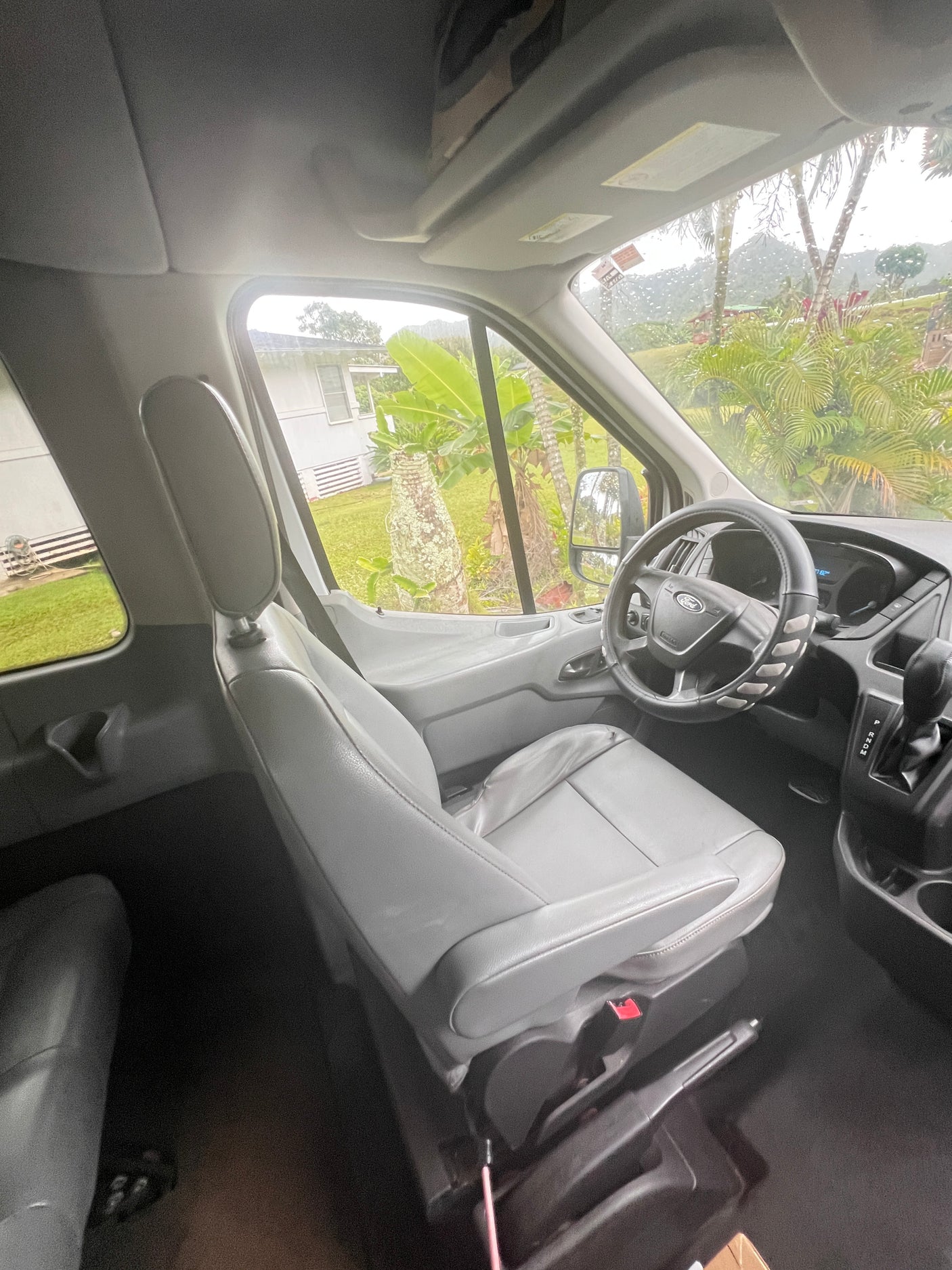 Spacious RV rental interior: Ford van cockpit with gray seats and a rainy tropical landscape view.