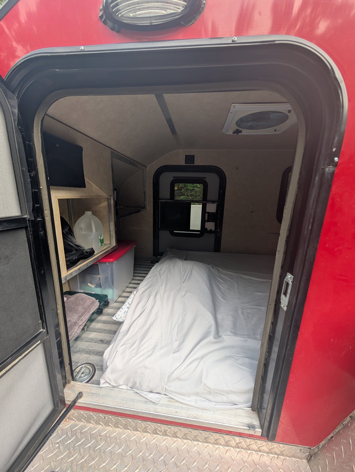 Inside a cozy RV rental: bed, storage shelves, and vent visible from the open doorway. Perfect for adventurers.