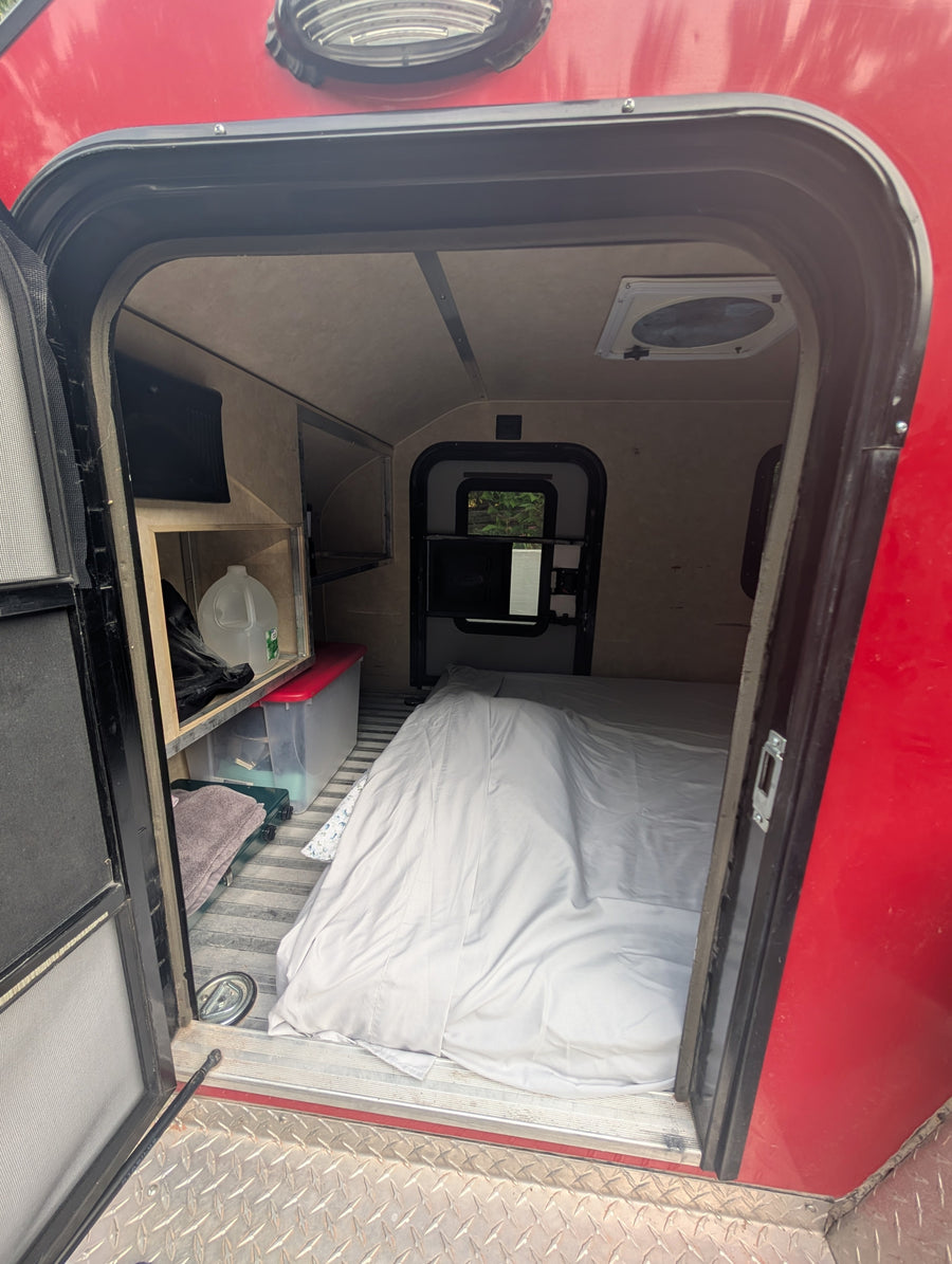 Inside a cozy RV rental: bed, storage shelves, and vent visible from the open doorway. Perfect for adventurers.