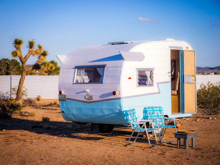 Charming blue & white vintage camper rv rental in the desert. Relax outside with the included chairs and table.
