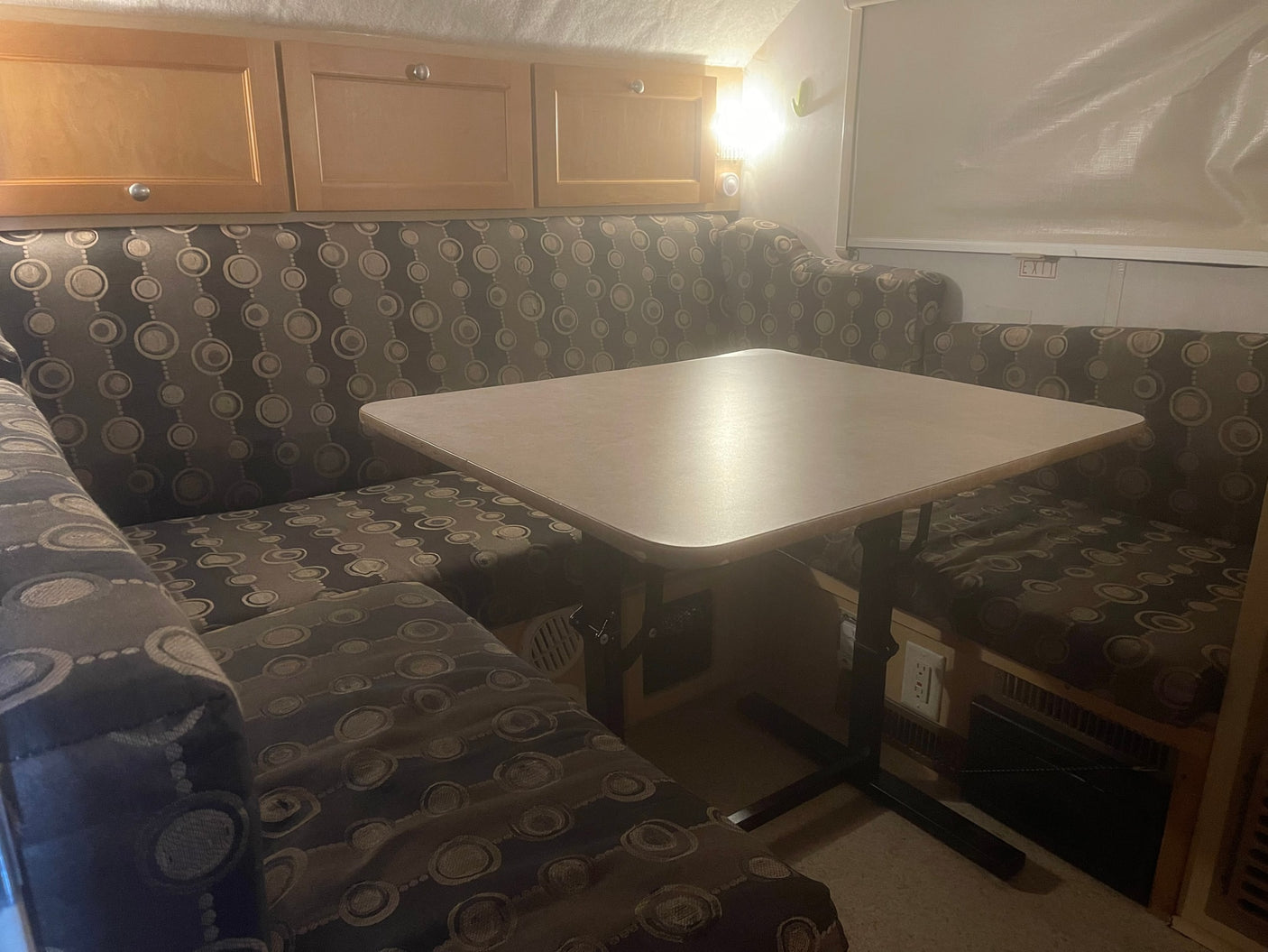 Cozy RV rental dinette features patterned cushion benches, a light-colored table, and wooden overhead cabinets.
