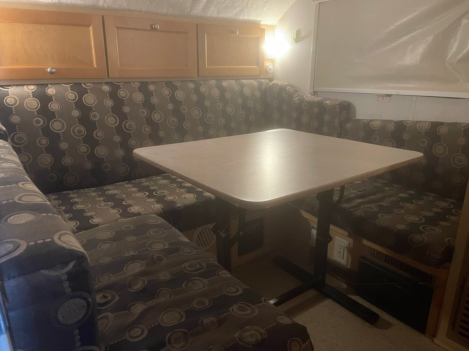 Cozy RV rental dinette features patterned cushion benches, a light-colored table, and wooden overhead cabinets.