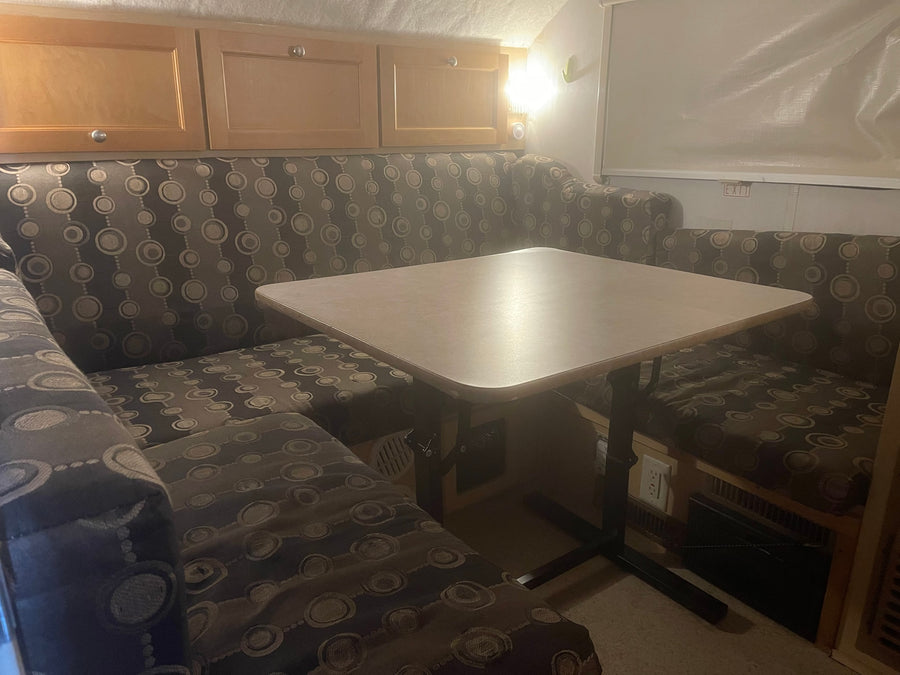 Cozy RV rental dinette features patterned cushion benches, a light-colored table, and wooden overhead cabinets.