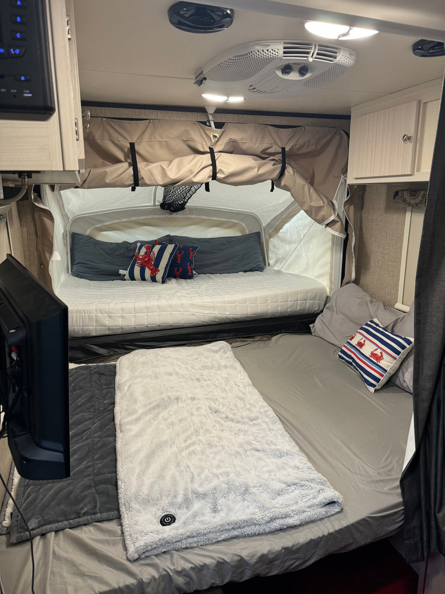 RV rental interior: A cozy space featuring two sleeping areas (one pop-out), comfy blankets, TV, and an overhead AC unit.