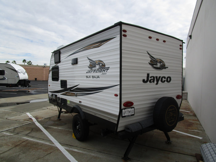 This Jayco Jay Flight SLX BAJA travel trailer, a potential RV rental, is shown parked from its side and rear view.